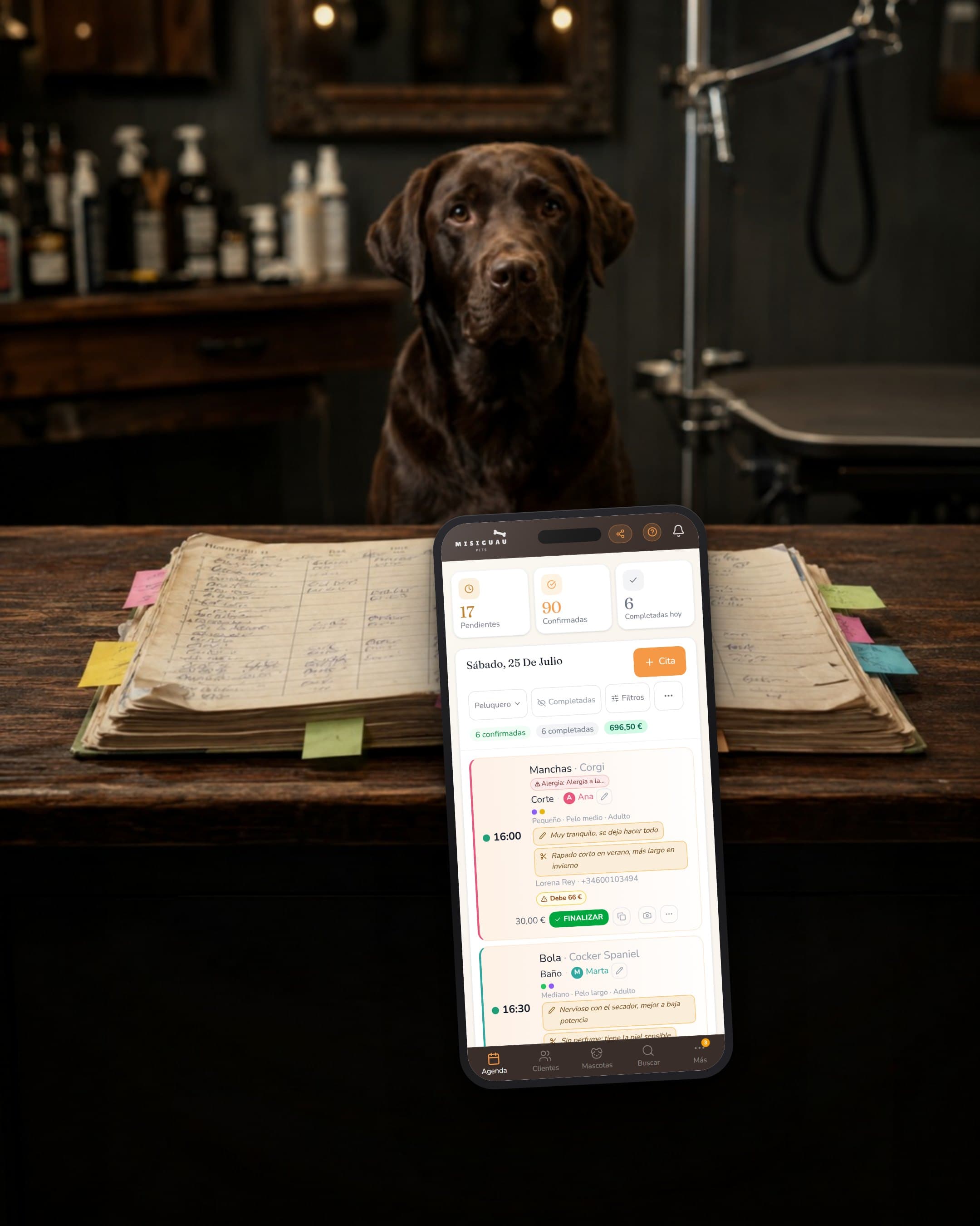 El mostrador de una peluquería canina: la agenda de papel escrita a mano y llena de post-its, y delante un móvil con la agenda de petgroomer, ordenada, con las citas del día y lo cobrado.